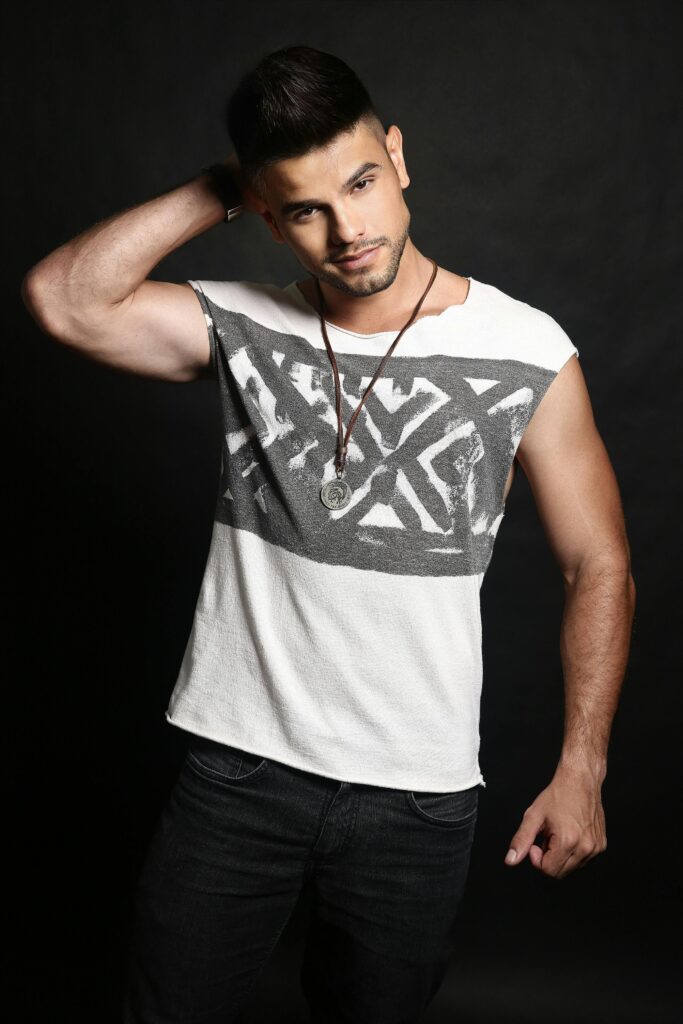 Stylish portrait of a man posing in a graphic tank top with necklace against a black background.